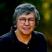 Photo of Donna Loring, dark collared shirt, short hair, glasses, blurred background