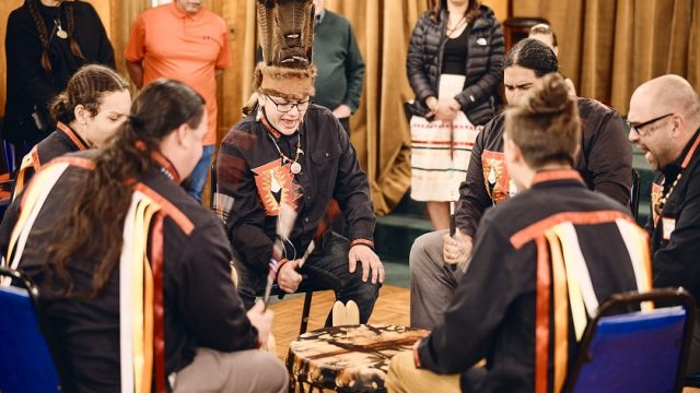 Drummers performing at Rising Voices. Six men seated around a drum performing and signing