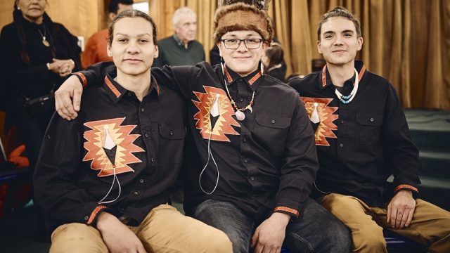Three Indigenous men wearing black and orange shirts