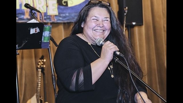 Chief Clarissa Sabattis of the Houlton Band of Maliseet Indians. Chief Clarissa Sabattis of the Houlton Band of Maliseet Indians stands at a microphone smiling wearing black sweater